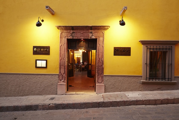 A yellow building with an entrance featuring a stone archway. There are signs on the wall indicating 'Aperi Restaurant' and 'De Casa'.