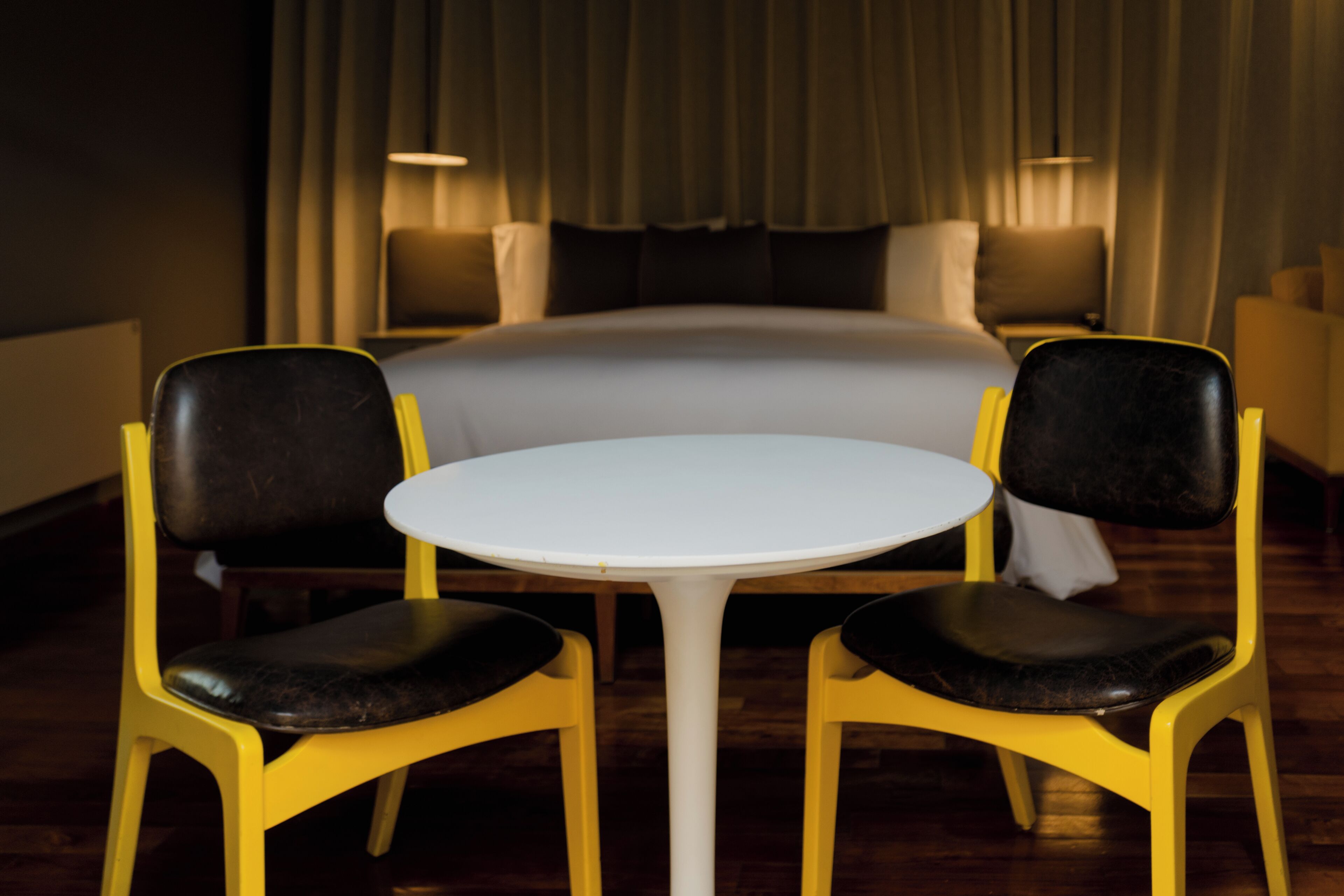 Een hotelkamer met een bed, twee stoelen, een tafeltje en een gordijn.