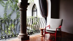 A balcony with a red chair, a stone pillar, and a view of greenery through a metal railing. - Dos Casas Hotel & Spa (San Miguel de Allende)