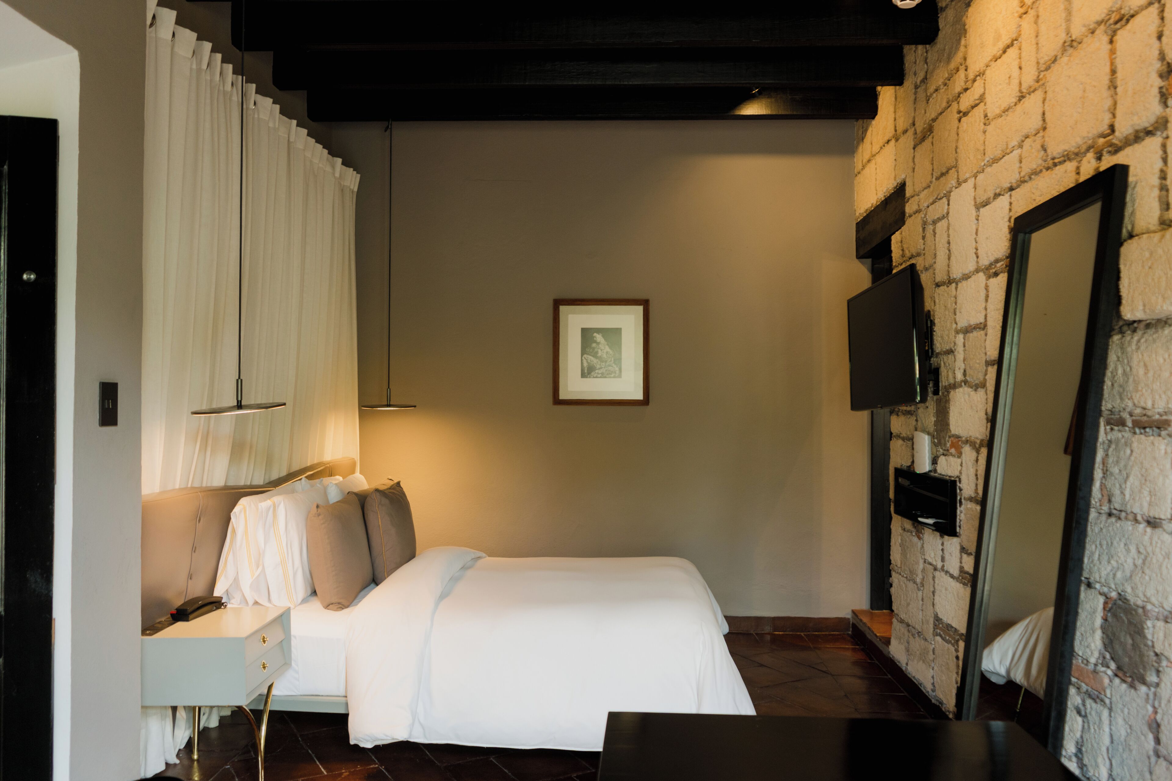 A hotel room with a bed, bedside table, lamp, and a framed picture on the wall.