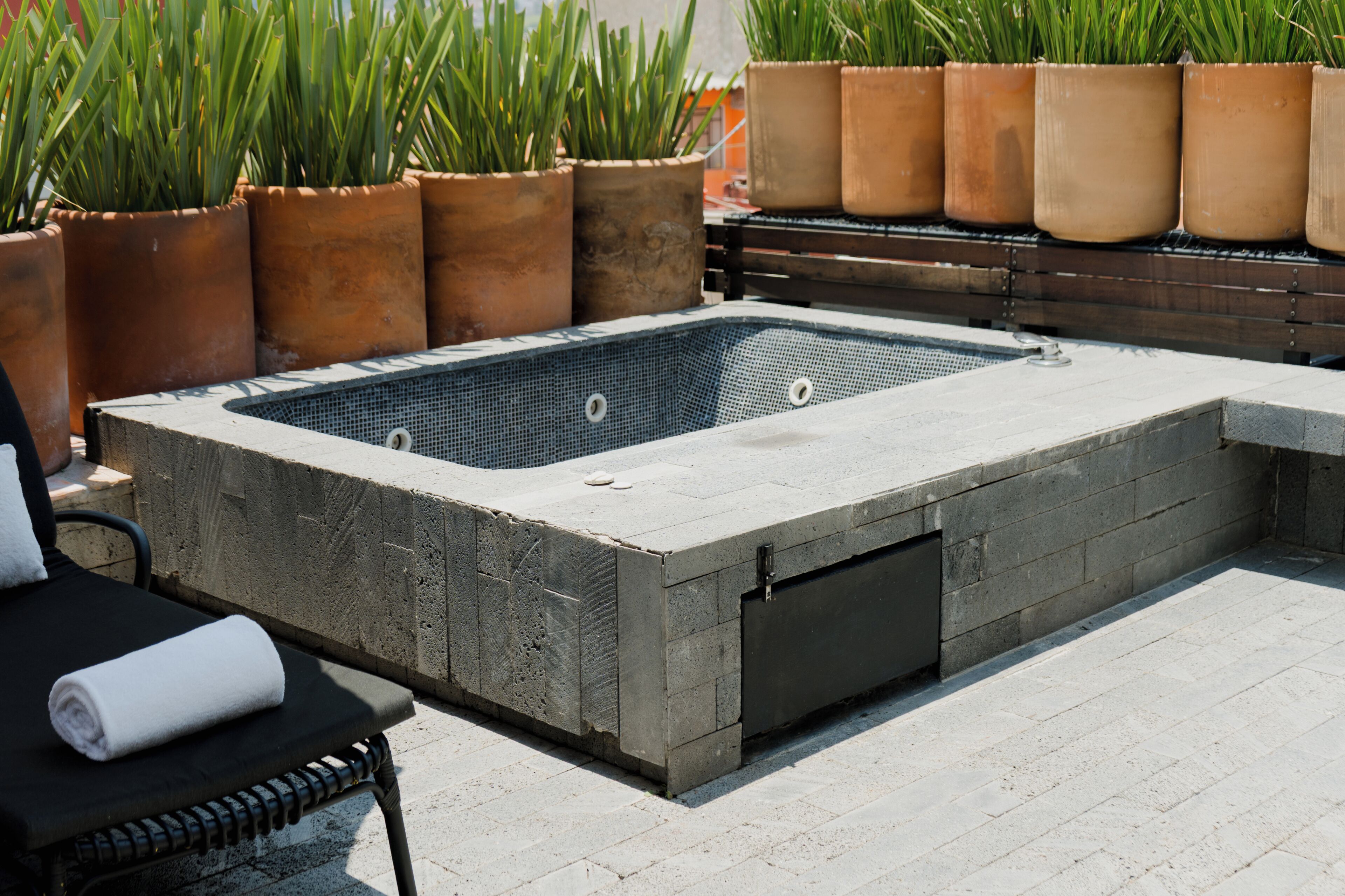 Un bain à remous rectangulaire doté d’un fond en treillis, entouré de plantes en pot et bordé d’une terrasse en bois.