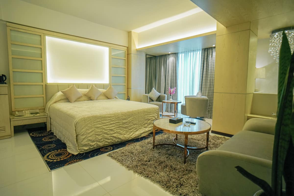 Una habitación de hotel con una cama, una mesa de centro redonda, una silla, un escritorio y un ventanal grande.