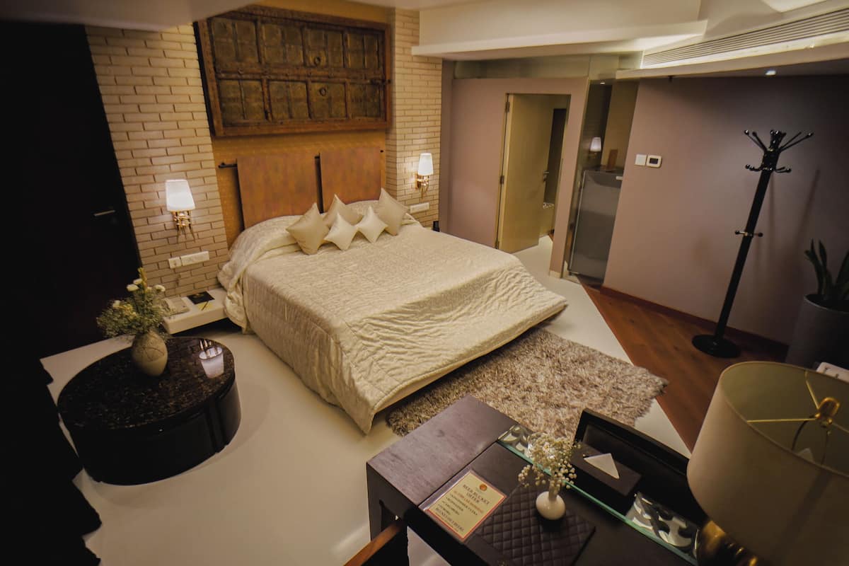 Un dormitorio con una cama grande, una mesita de noche con lámpara, una luz en la pared y un perchero.