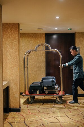 A hotel room with a luggage cart, a wooden door, and a patterned carpet. - Peninsula Grand Hotel (Mumbai)