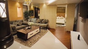 A modern living room with a sofa, coffee table, and a bed with a brick wall. - Peninsula Grand Hotel (Mumbai)