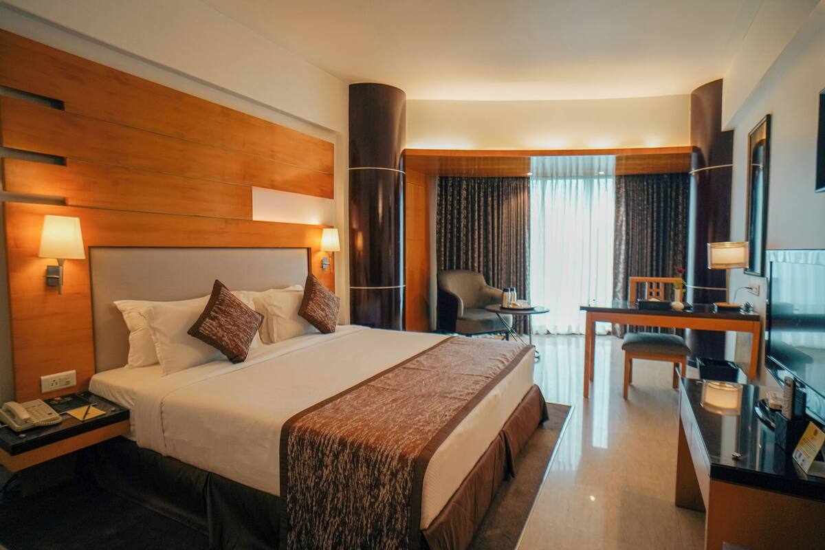 Habitación de hotel con una cama grande, mesitas de noche, un escritorio, una silla, un televisor y una ventana con cortinas.