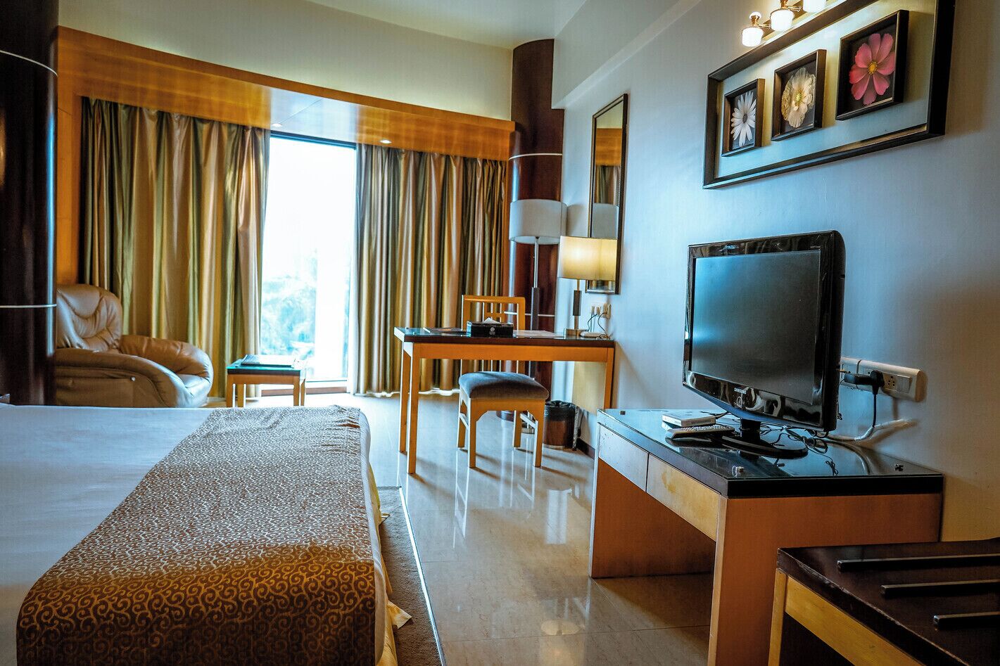 A hotel room with a bed, desk, television, and large windows with curtains.
