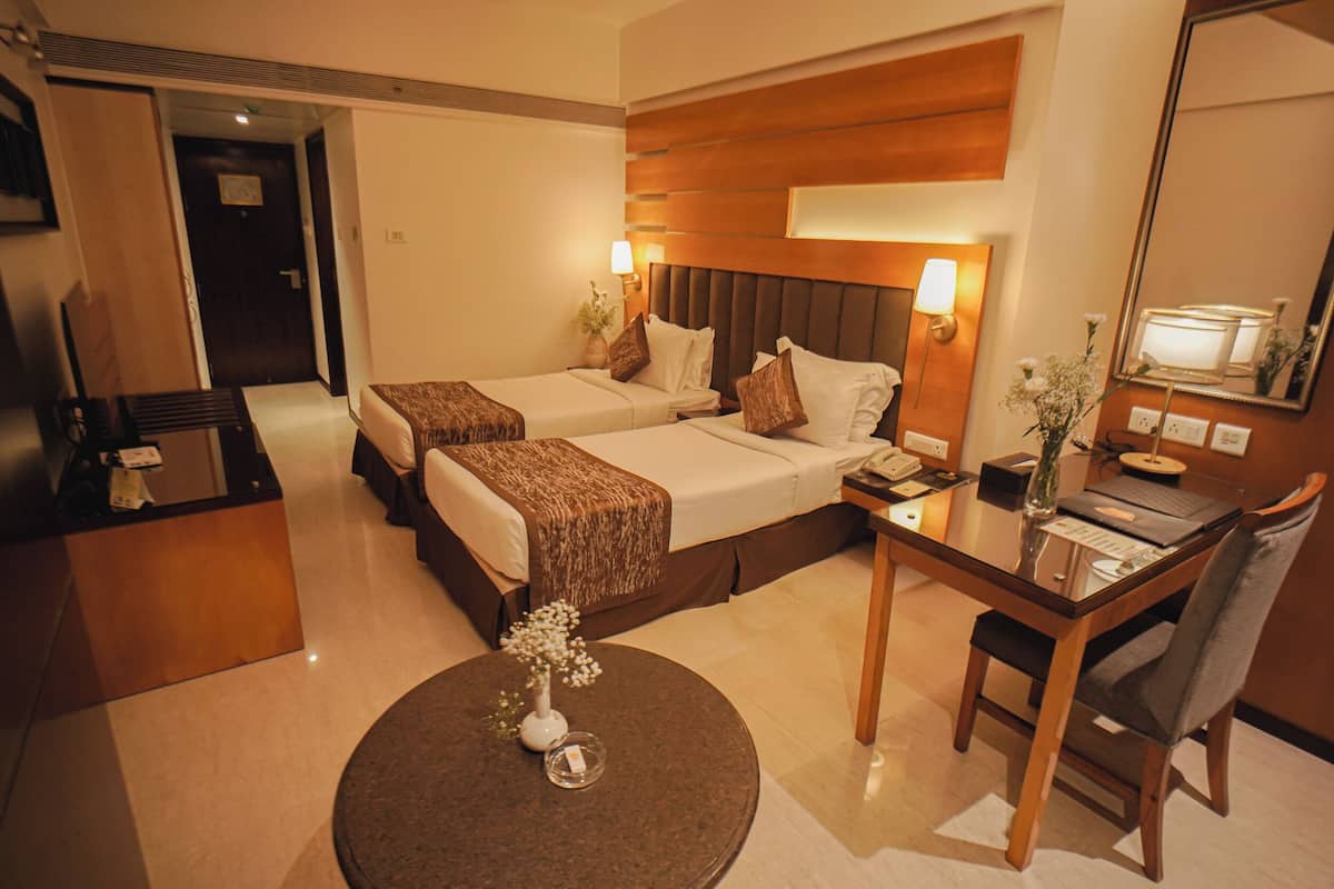 Habitación de hotel con dos camas, un escritorio, una silla, una mesa redonda y un espejo.