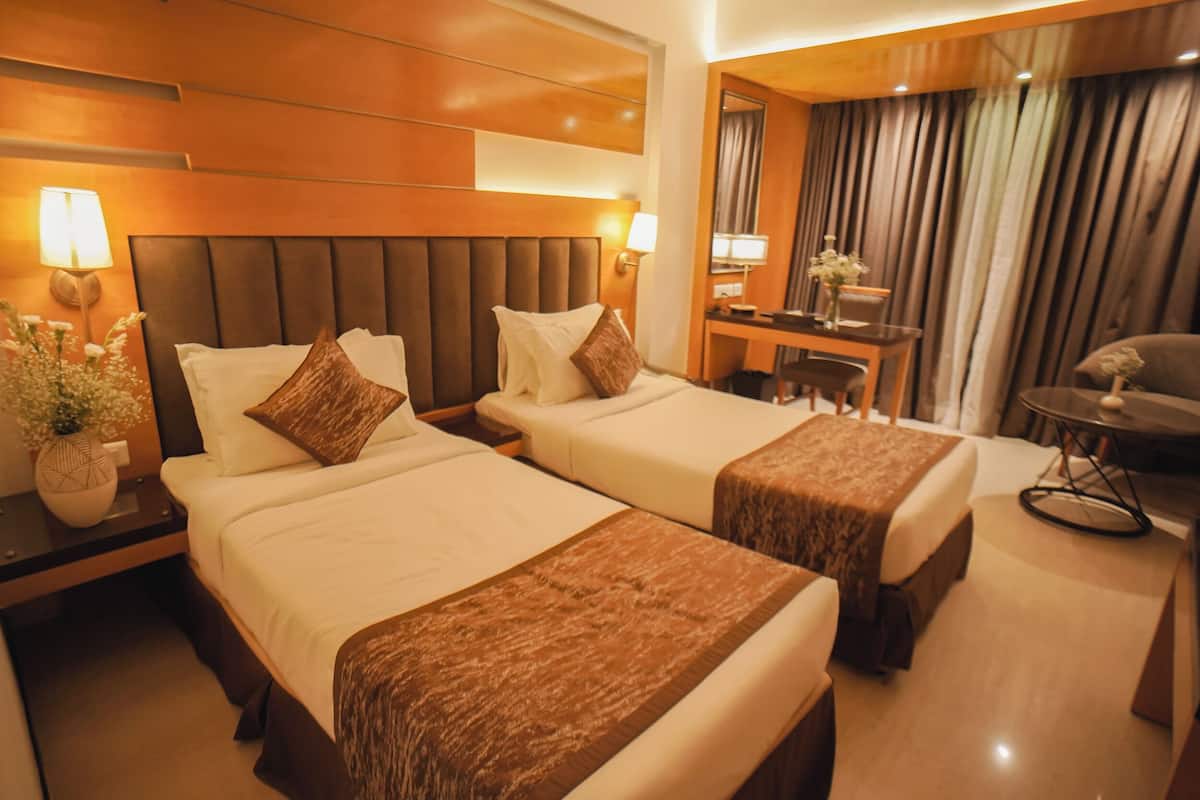 Una habitación de hotel con dos camas, un escritorio, una silla, una lámpara y un espejo.
