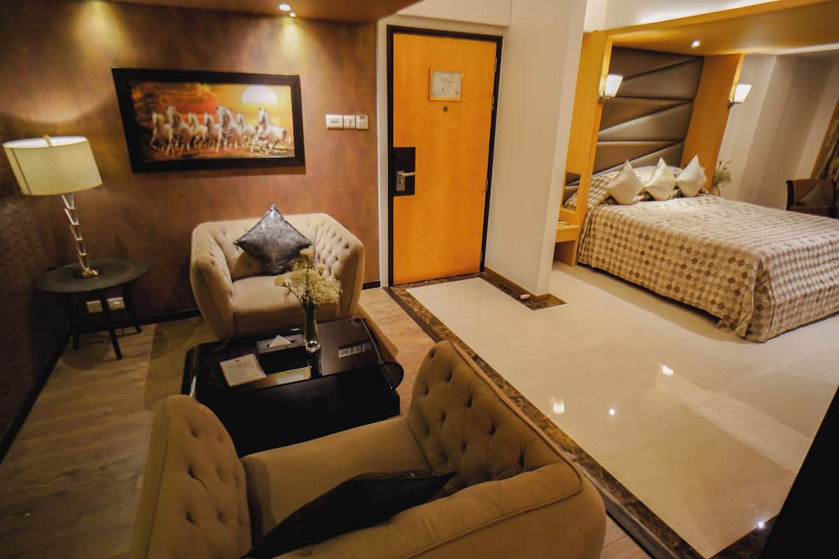 Una habitación de hotel con una cama, un sofá, una mesita con una lámpara y un cuadro en la pared.