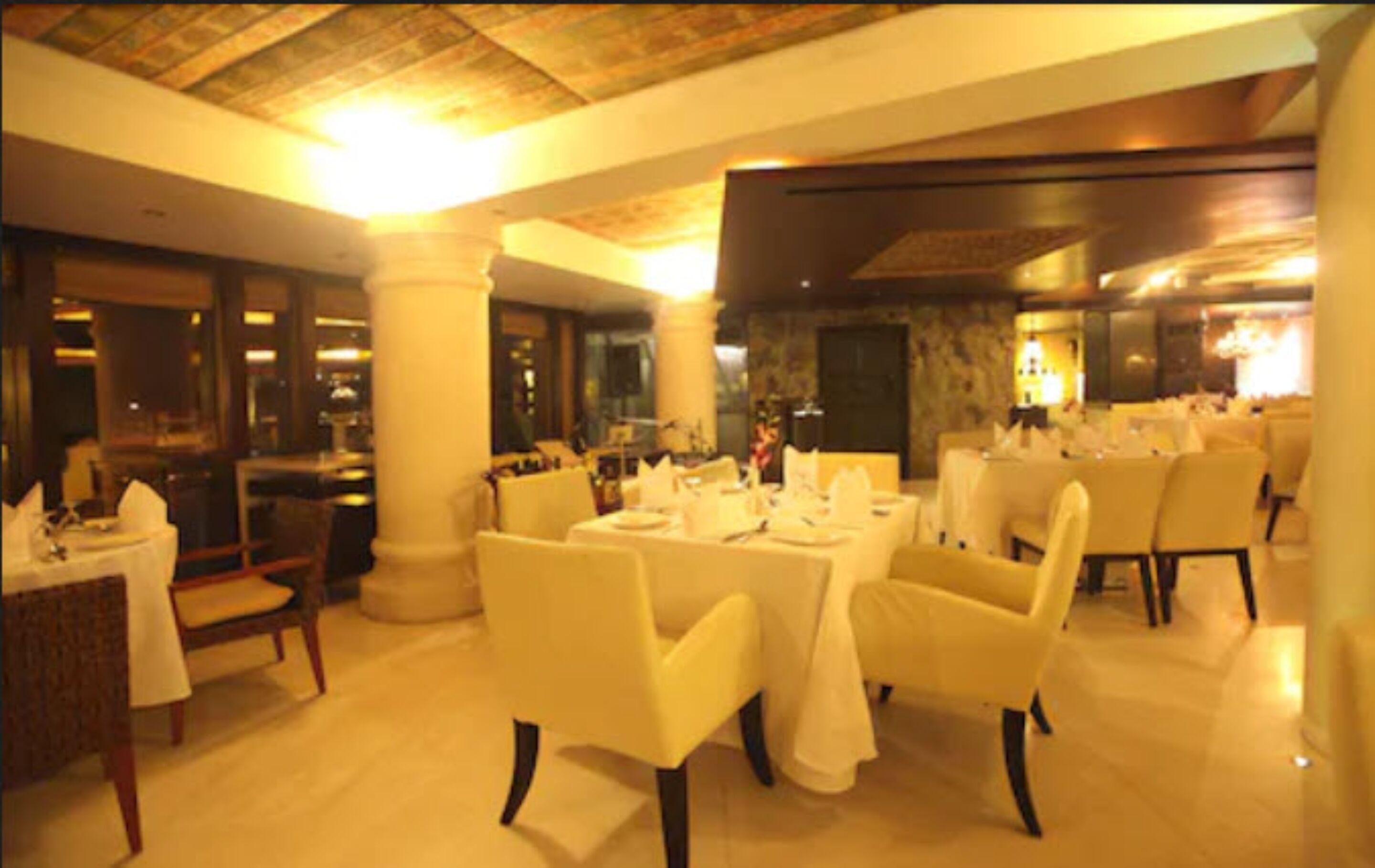 A restaurant with tables set for dining, white chairs, and a warm, well-lit interior.