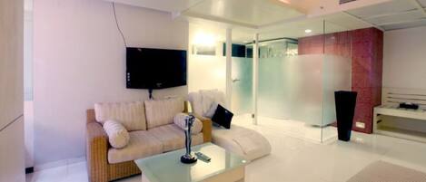 A modern living room with a sofa, coffee table, TV, and a glass shower area.