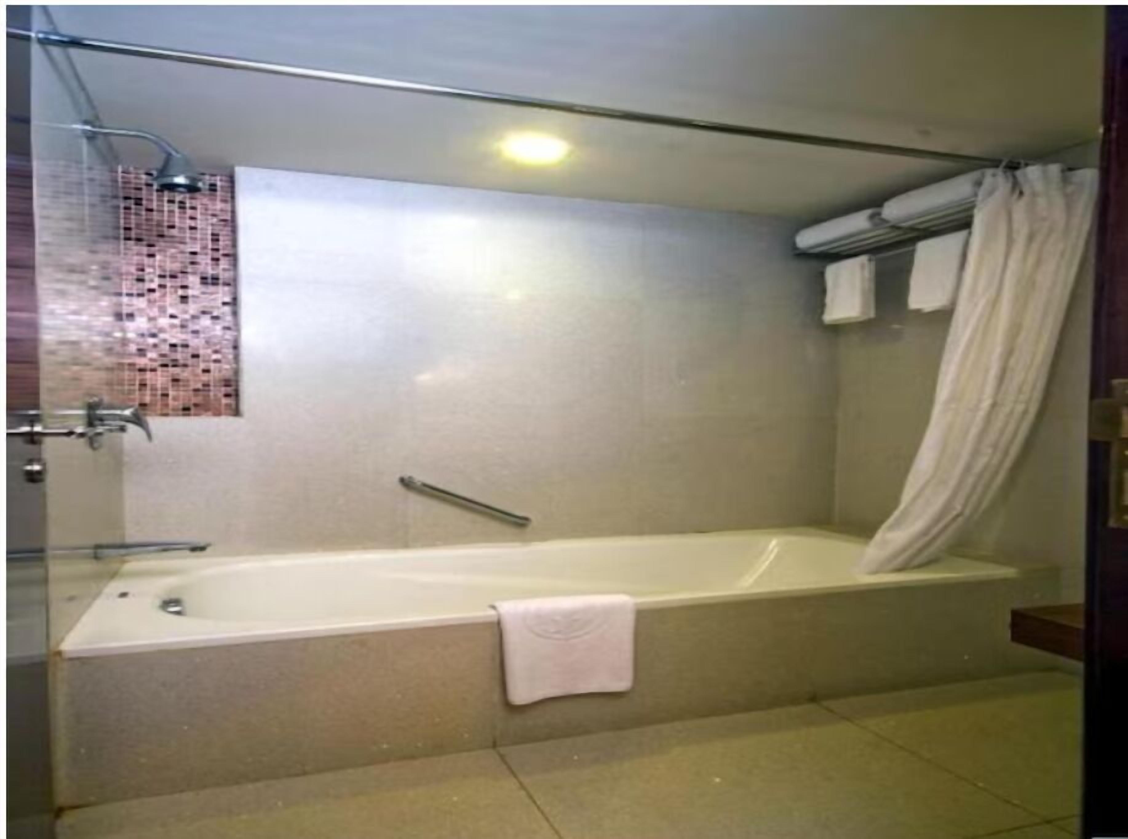 A bathroom with a bathtub, a shower, a glass-enclosed shower area, and a tiled wall.