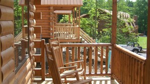 A wooden deck with a rocking chair, a covered porch, and a view of a vehicle in the background.