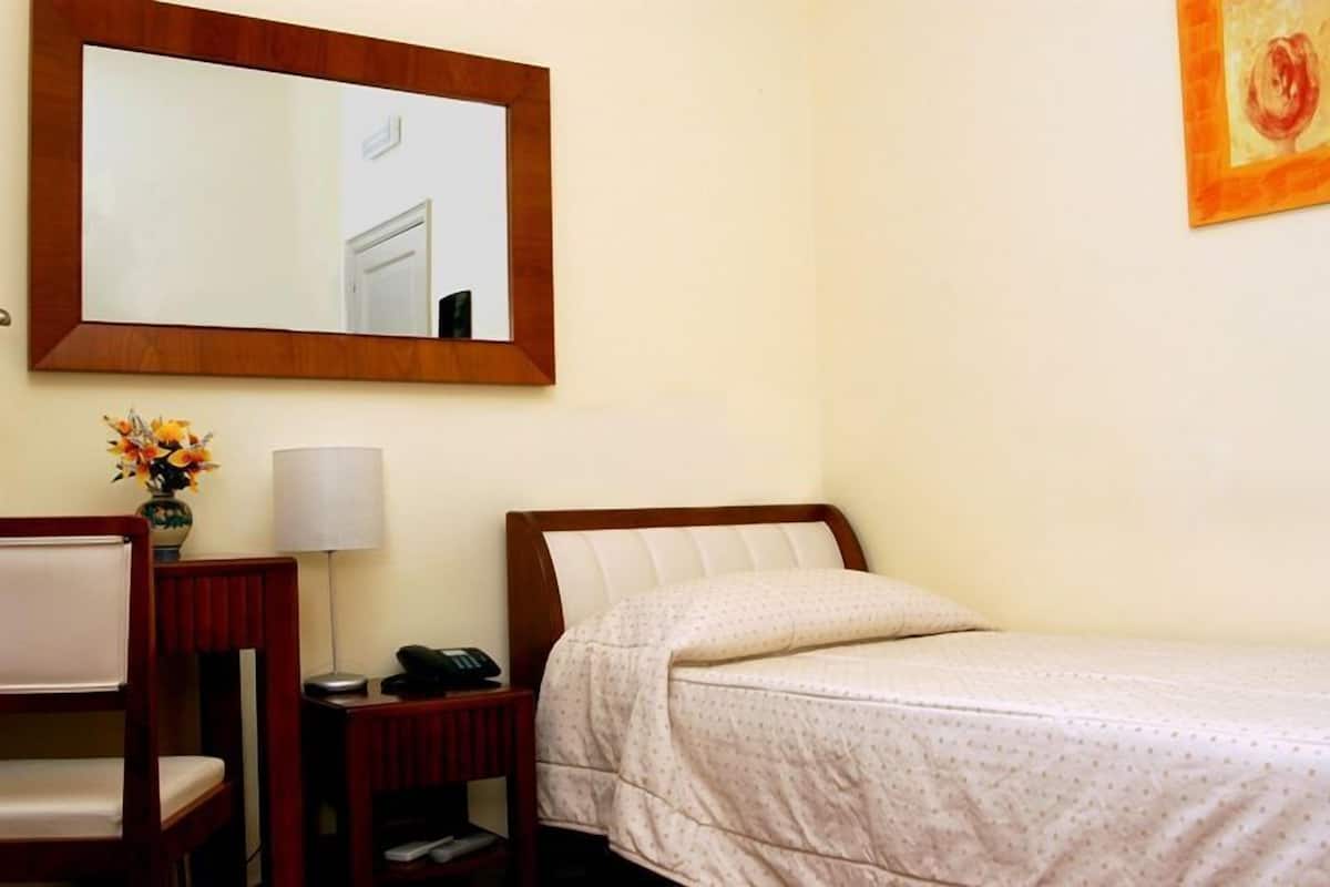 Habitación de hotel con cama, escritorio con lámpara, silla, teléfono y espejo en la pared.