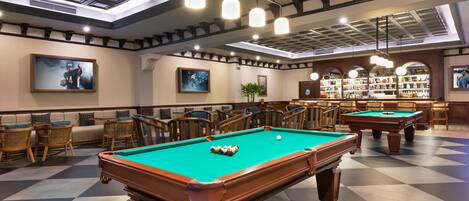 Une table de billard recouverte d’un drap vert, entourée de chaises en bois et d’un canapé.