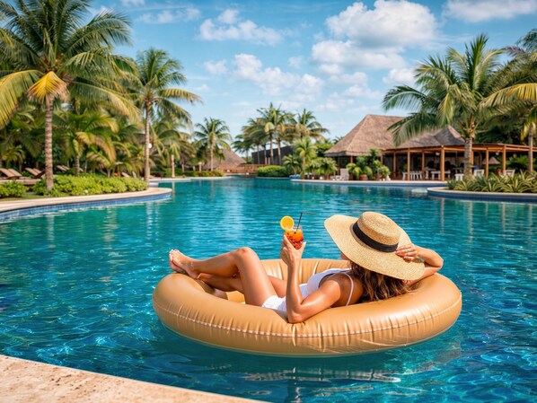A person relaxing on an inflatable ring in a pool surrounded by palm trees and a thatched-roof structure. - Valentin Imperial Rivera Maya All Inclusive - Adults Only (Playa del Carmen)