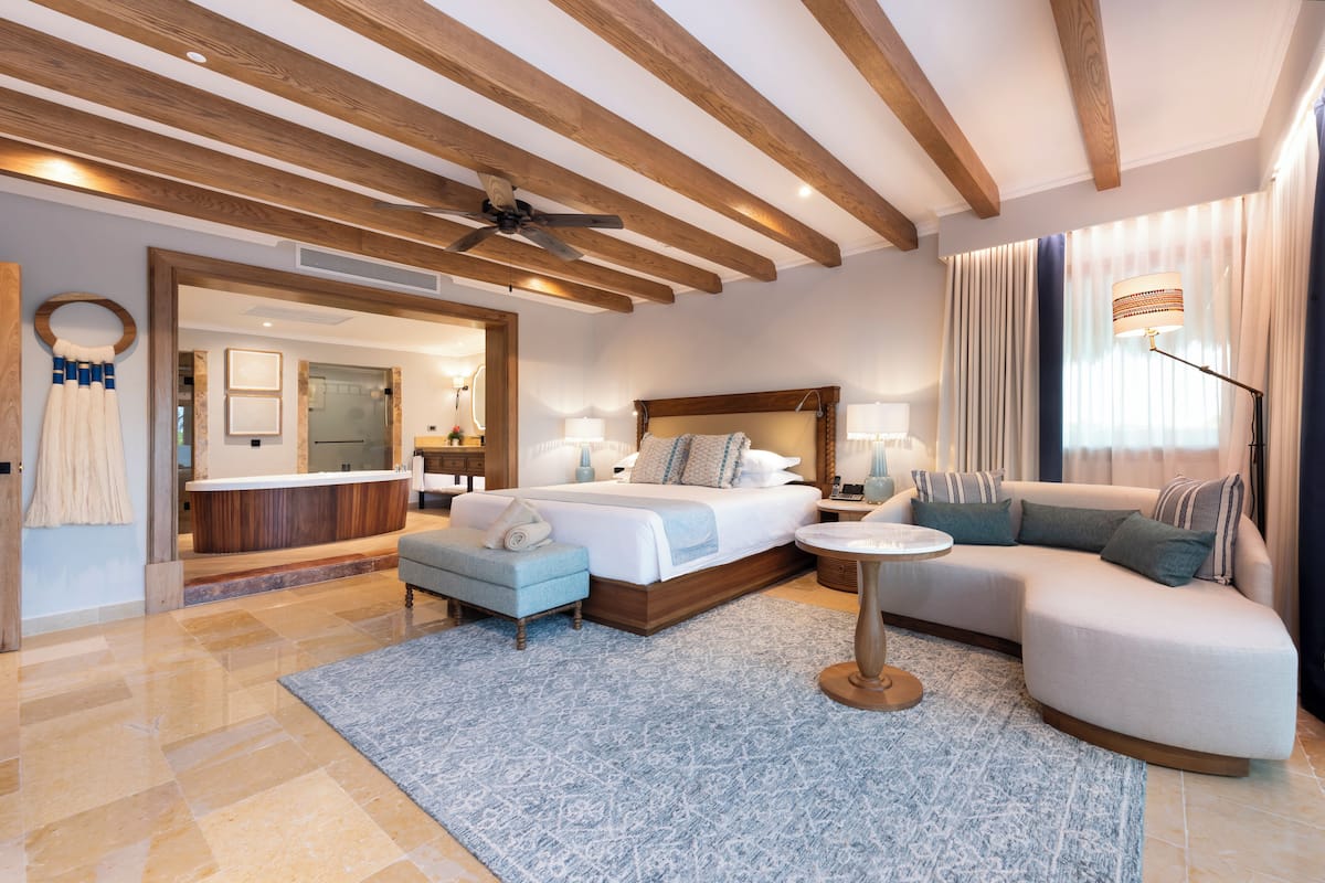 A modern hotel room with a large bed, a sofa, a small table, and a ceiling fan.