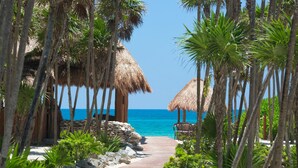 A wooden pathway leading to a beach with thatched-roof structures and palm trees. - Valentin Imperial Rivera Maya All Inclusive - Adults Only (Playa del Carmen)