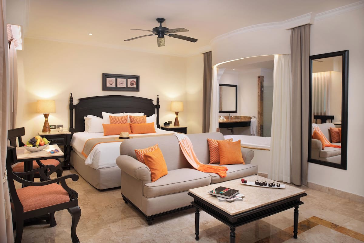 A hotel room with a bed, two sofas, a coffee table, a desk, and a chair.