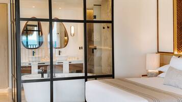 A modern hotel room with a large glass partition, a bed, a bedside table, a lamp, and a view of the sea through the glass.