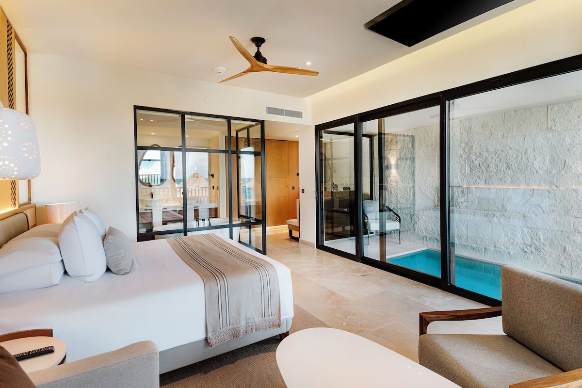 A modern hotel room with a large bed, a sitting area, and a view of an indoor pool.
