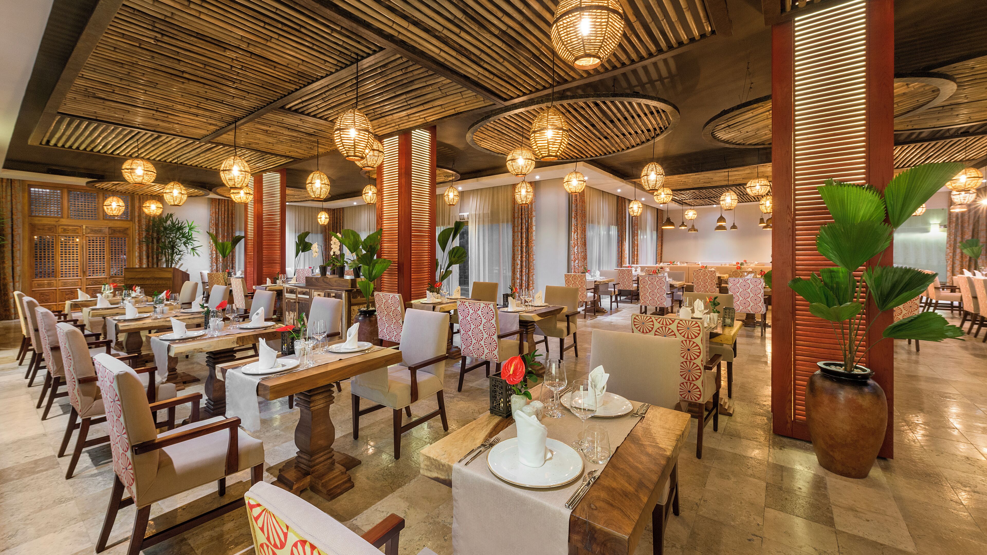 A spacious restaurant with multiple dining tables and chairs, bamboo ceiling design, and hanging light fixtures.