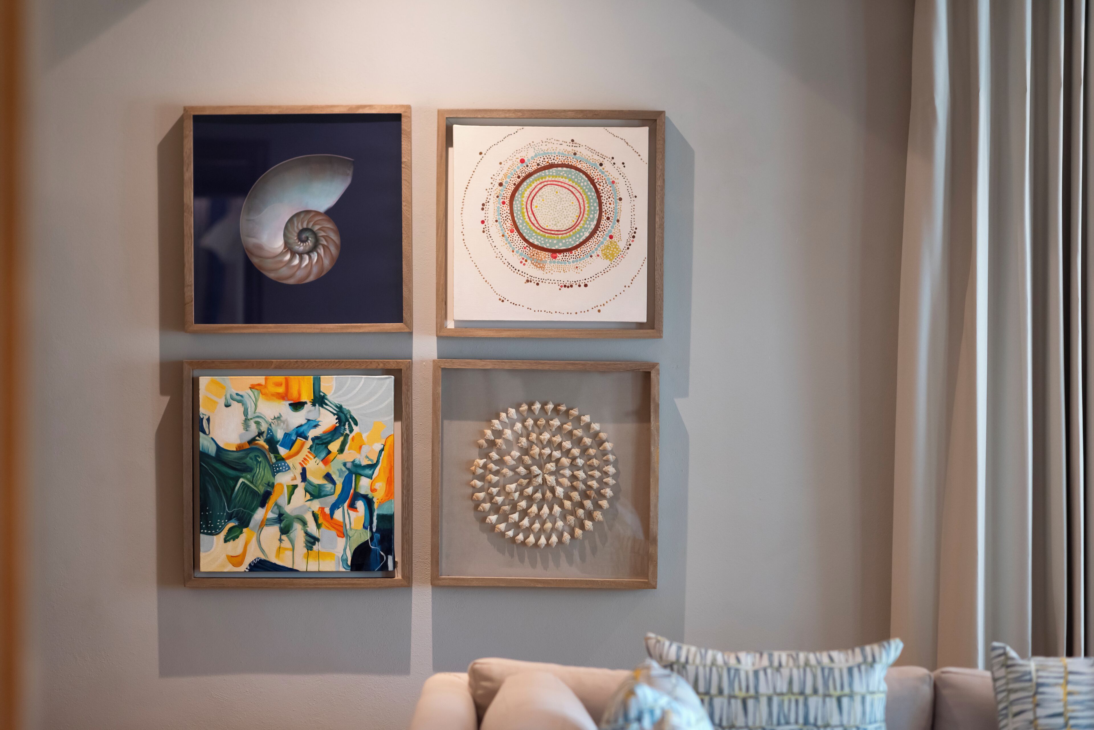 A wall with four framed artworks and a sofa with patterned cushions.