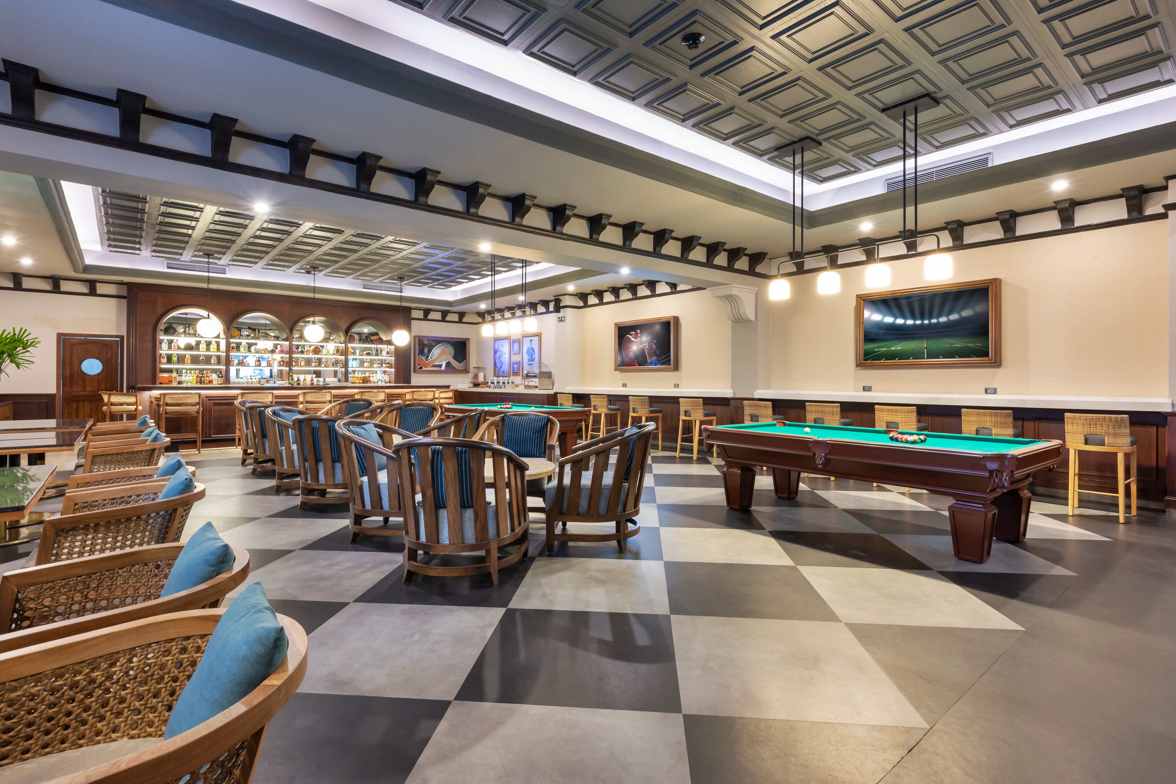 Een biljartkamer met meerdere tafels en stoelen, een bar met flessenkasten en lijstwerken aan de muren.