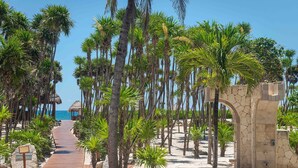 A wooden pathway leading to a beach with palm trees and a stone archway. - Valentin Imperial Rivera Maya All Inclusive - Adults Only (Playa del Carmen)