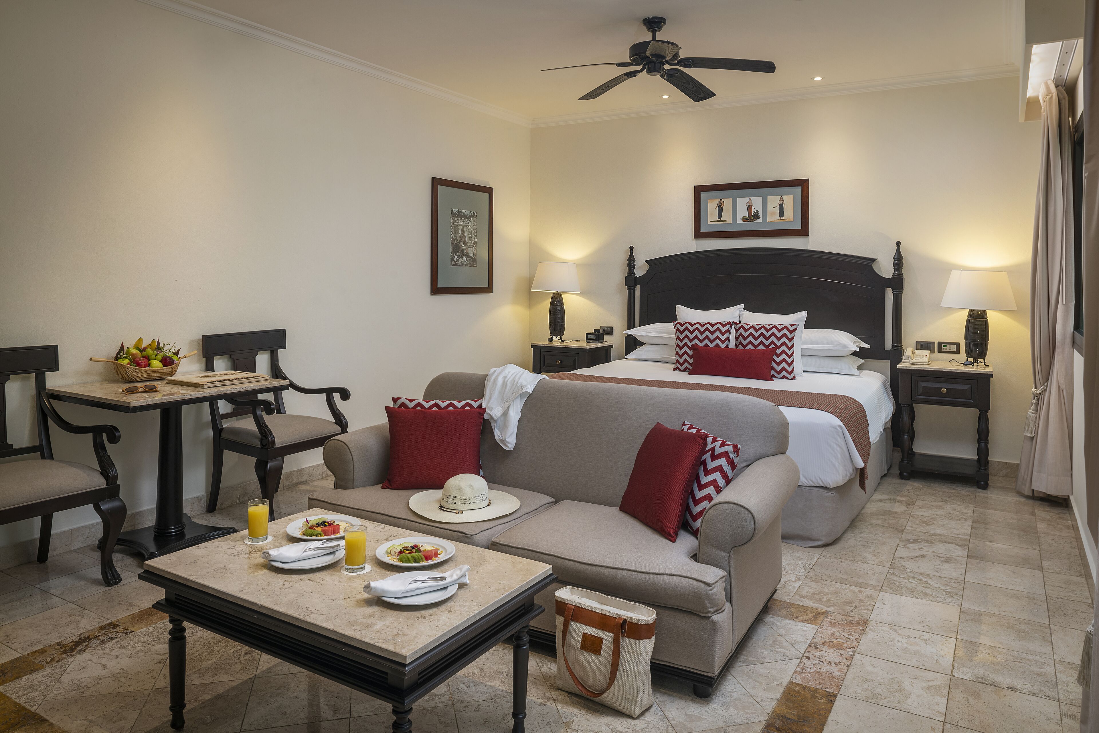 Een hotelkamer met een bed, een bank, een ontbijttafel en een kleine tafel met fruit.