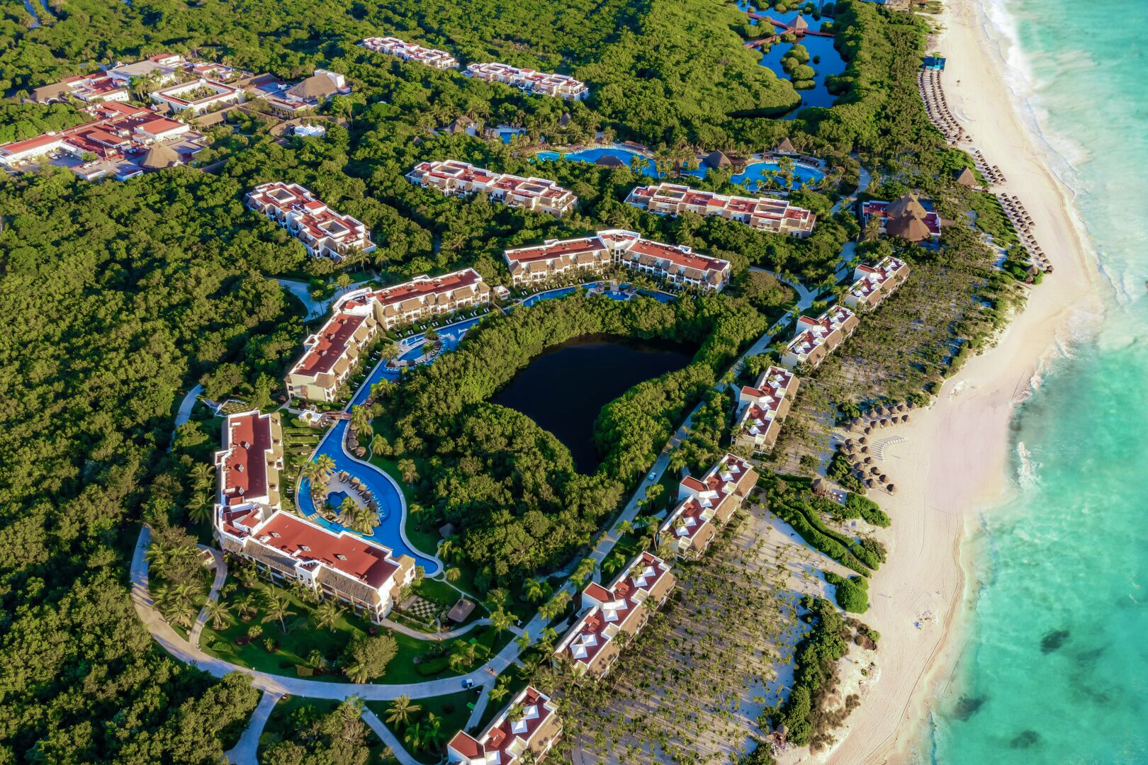 Vista aérea de un resort con varias construcciones, un elemento acuático central y una playa.