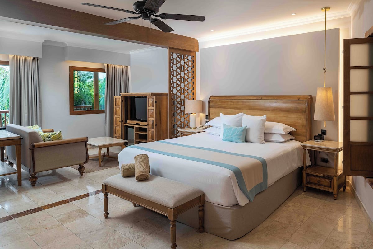 A hotel room with a large bed, a desk, a chair, a TV, and a ceiling fan.