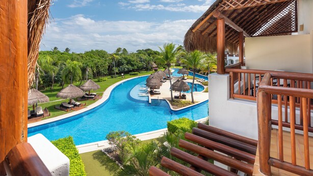 A resort pool area with a clear view of the pool, lounge chairs, and thatched umbrellas. - Valentin Imperial Rivera Maya All Inclusive - Adults Only (Playa del Carmen)
