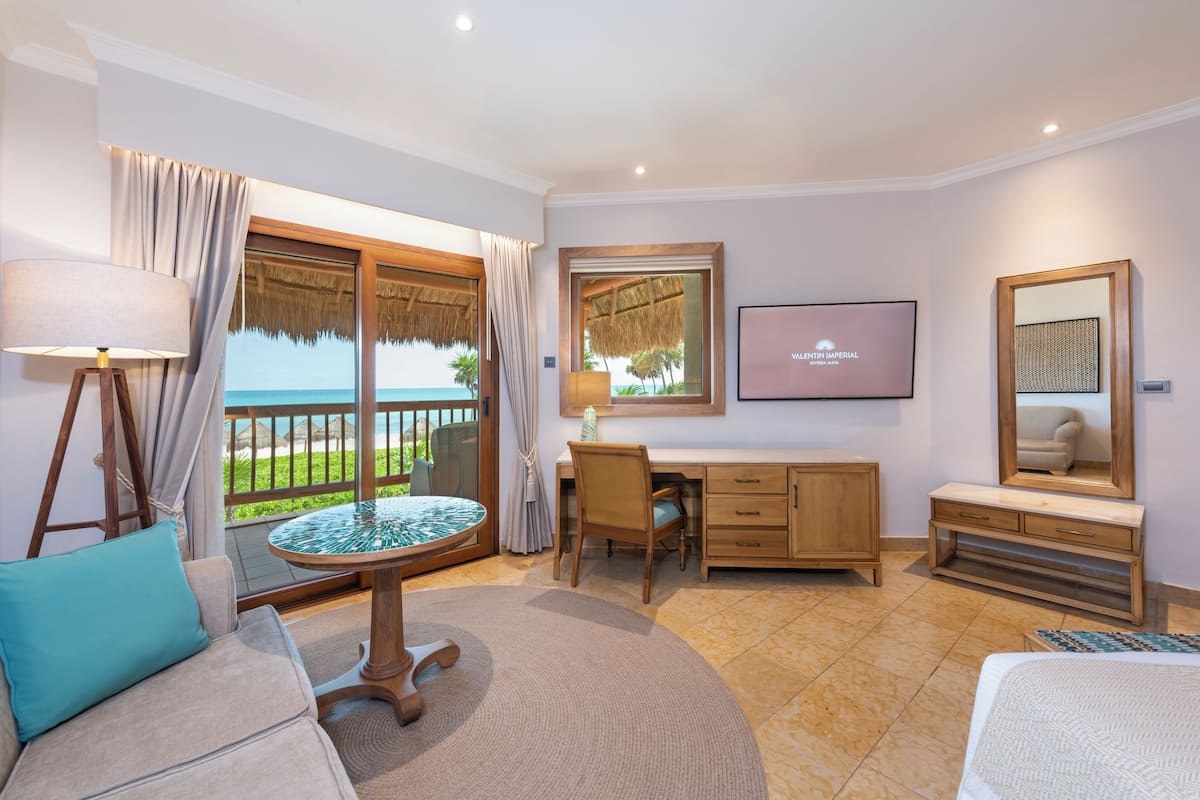 A hotel room with a balcony, a desk, a chair, a bed, and a TV.