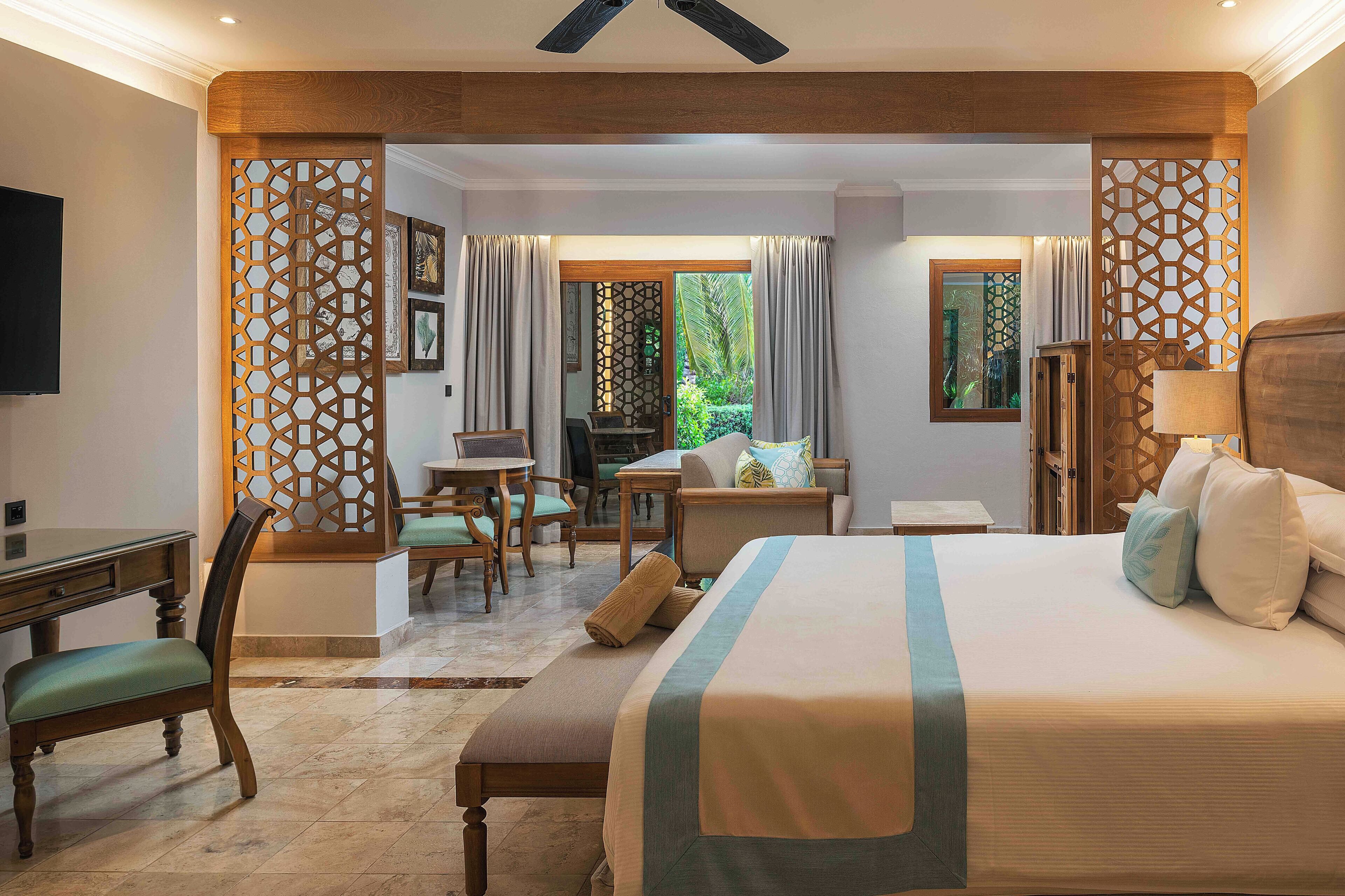 Une chambre d’hôtel avec un grand lit, un bureau et une chaise. On peut admirer la vue sur l’extérieur à travers une porte vitrée.