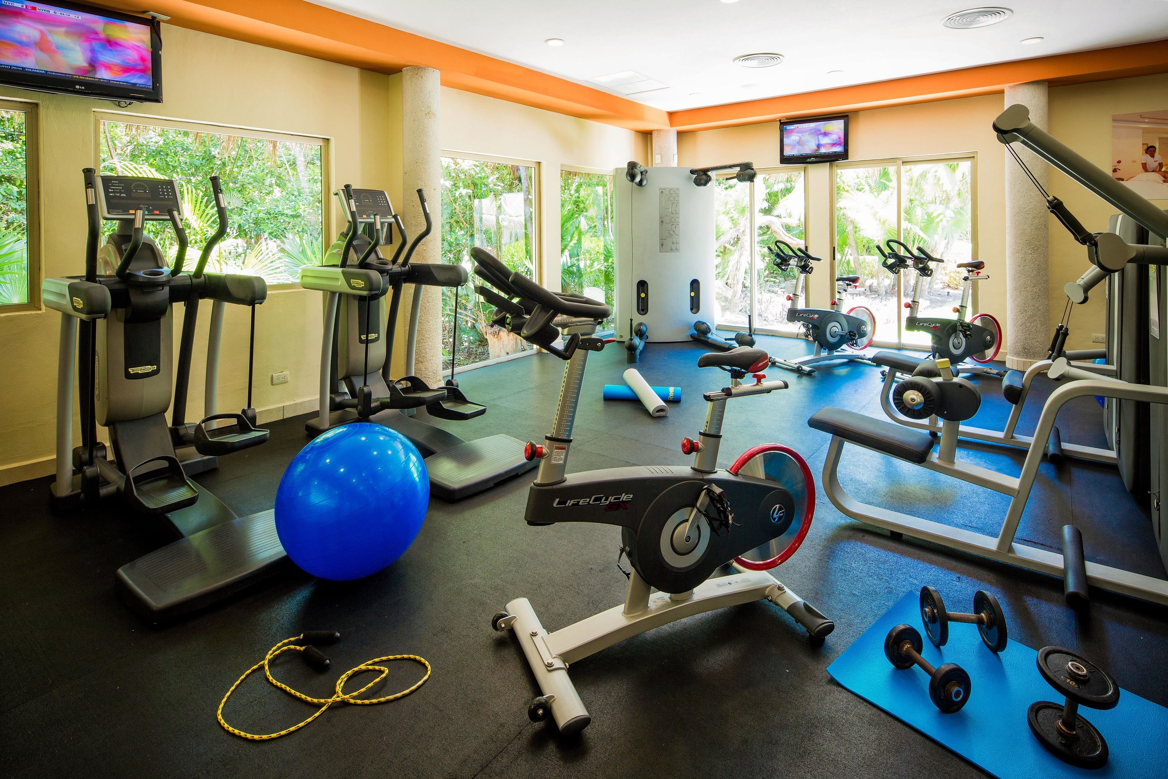 Een sportschool met loopbanden, elliptische trainers, een roeimachine, losse gewichten en trainingsballen.