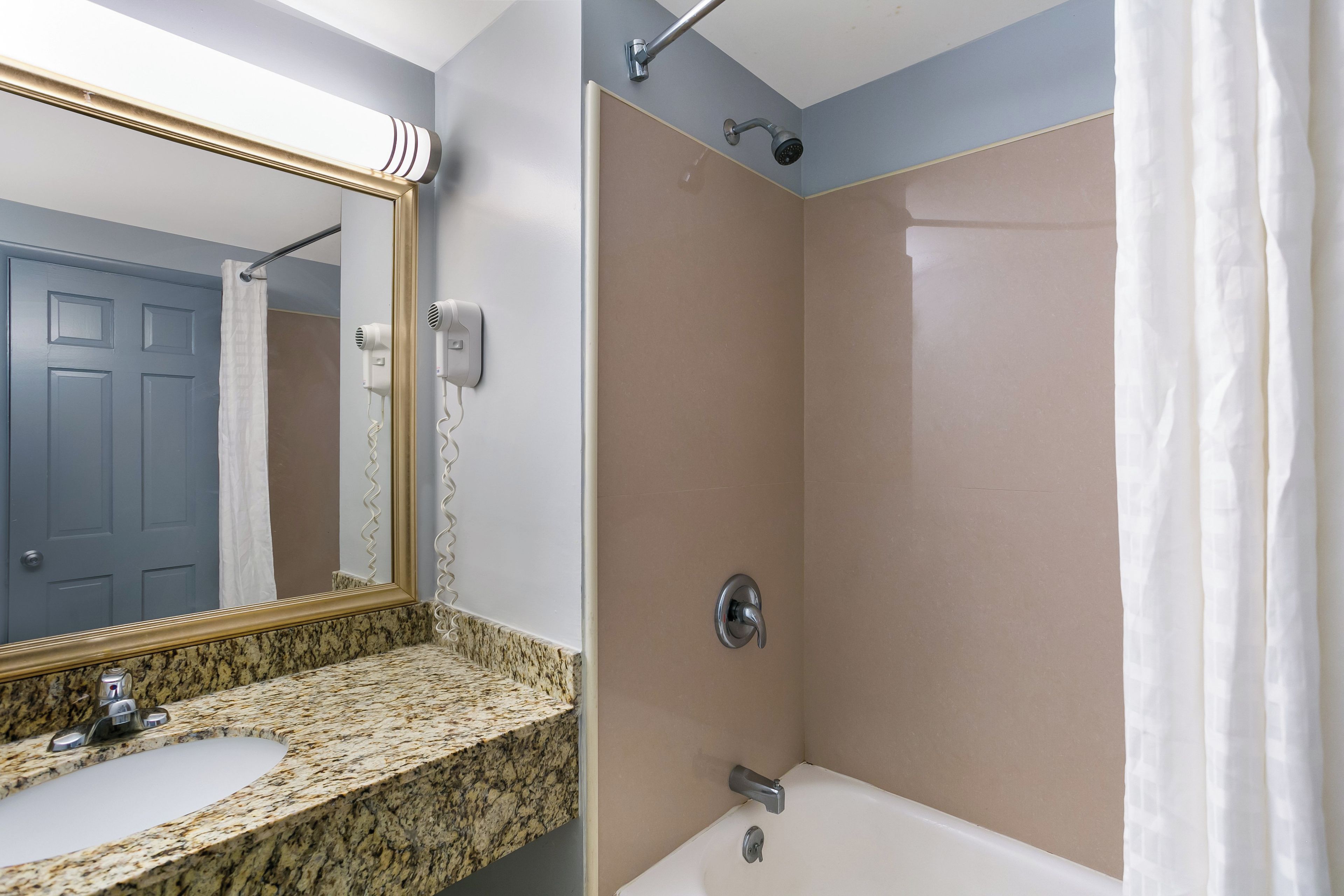 A bathroom with a granite countertop, a sink, a mirror, a shower with a curtain, and a door.