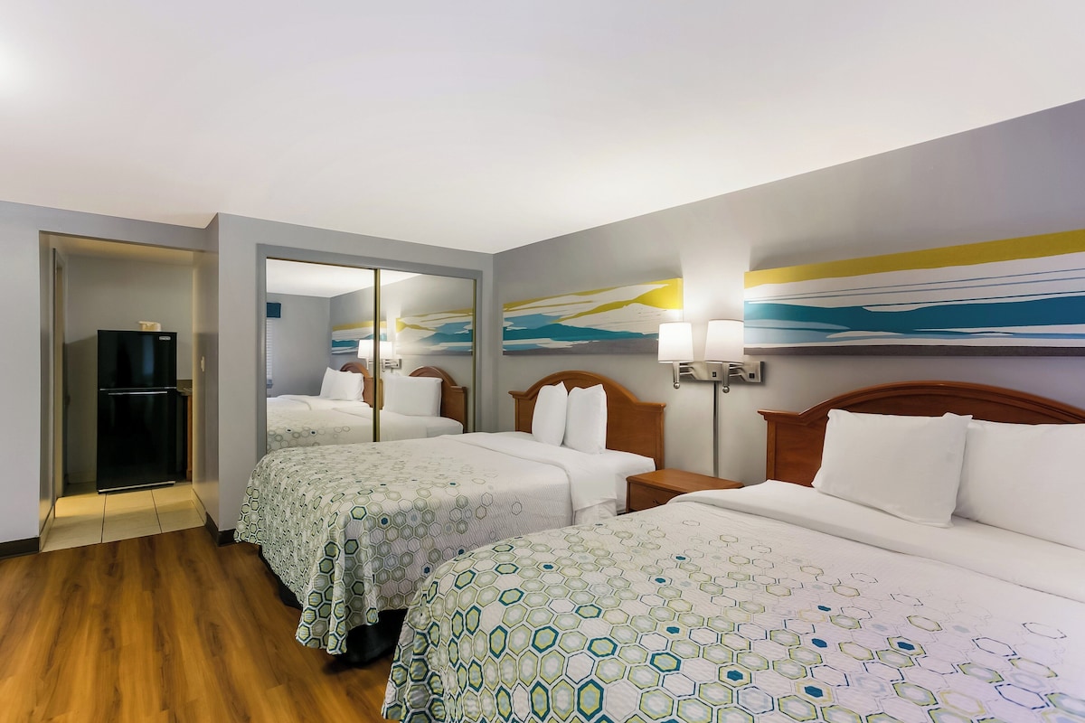 A hotel room with two beds, a refrigerator, a mirror, and a painting on the wall.