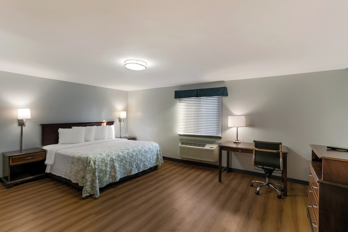 A hotel room with a bed, bedside tables, a desk, a chair, and an air conditioning unit.