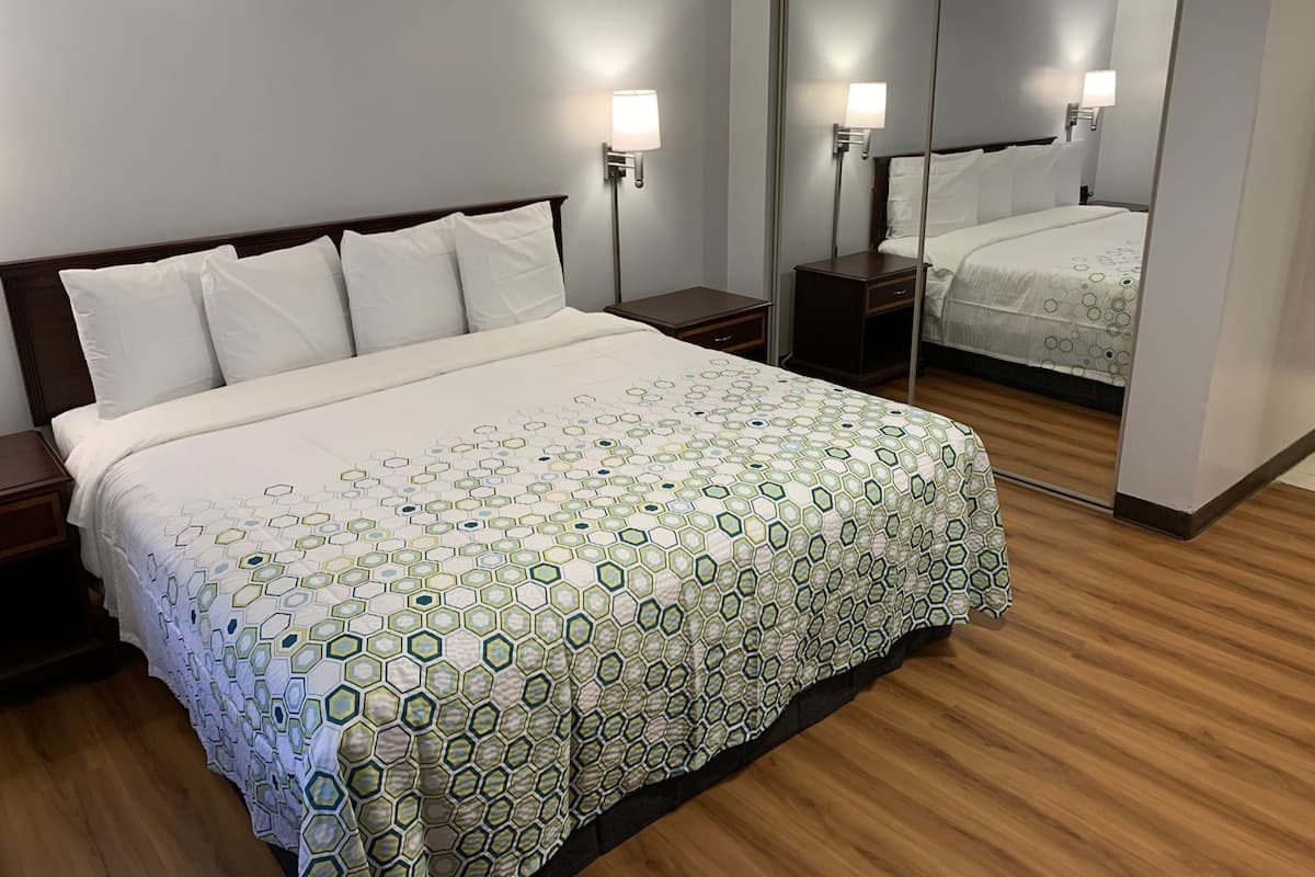 Et hotelværelse med en stor seng, et natbord, et sengebord, et spejl og en lampe på væggen.