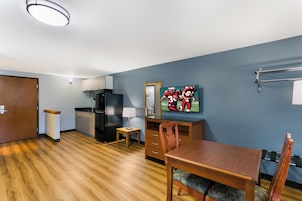 Habitación de hotel compacta con kitchenette, comedor y televisor mostrando un evento deportivo.