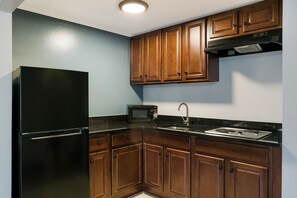 A kitchen with wooden cabinets, a black refrigerator, a microwave, and a stainless steel sink. - HomeTowne Studios by Red Roof Denver - Lancaster County (Denver)