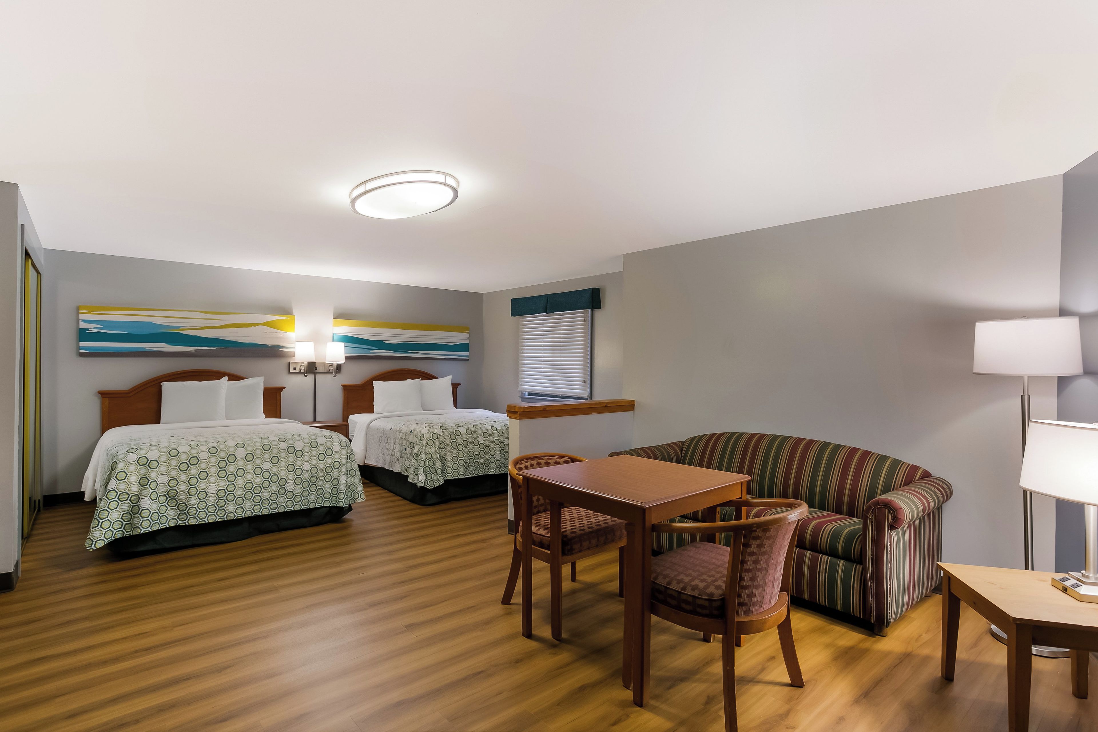 A hotel room with two beds, a dining table, a sofa, and a lamp.