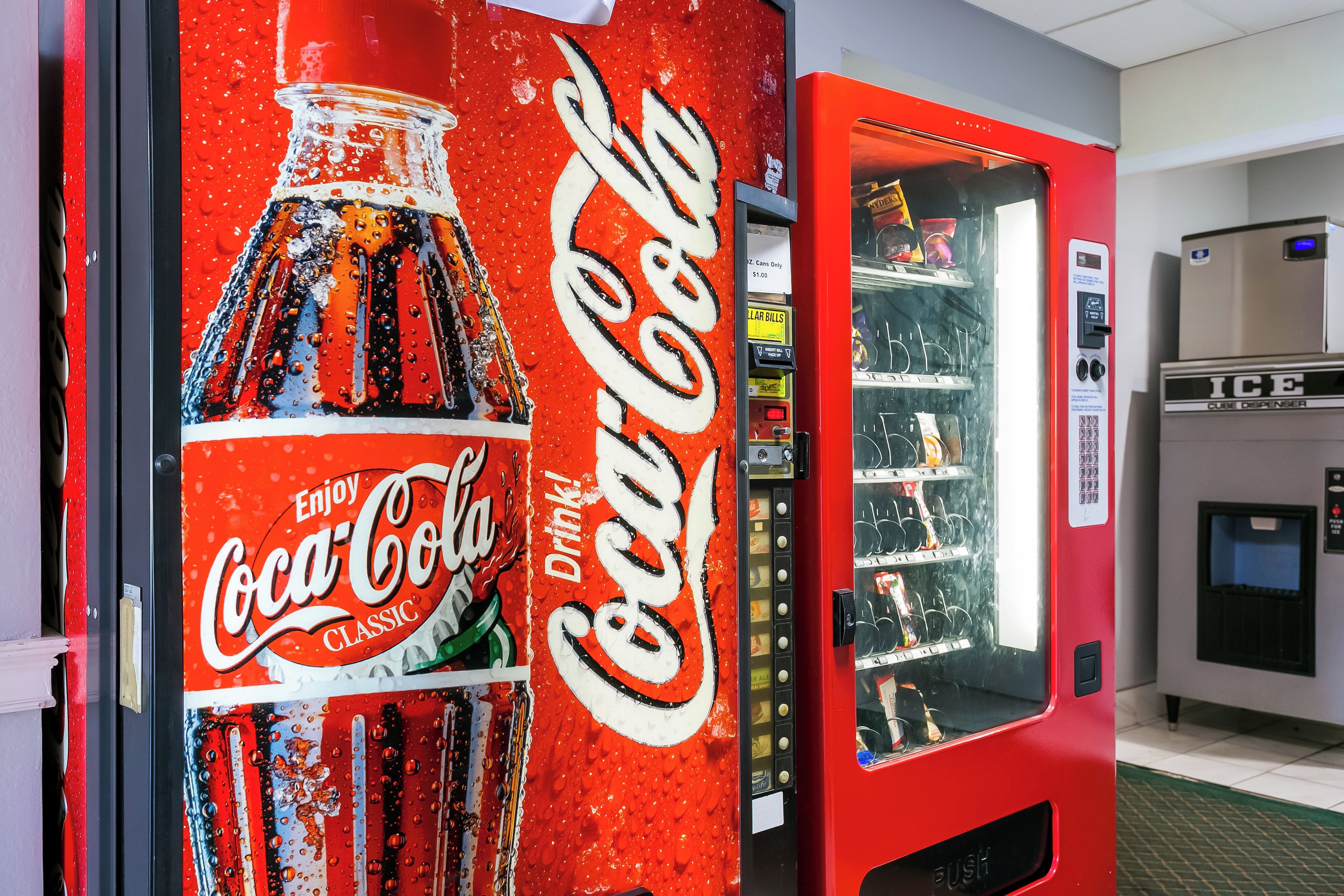 Un distributeur automatique de Coca-Cola doté d’une grande affiche publicitaire, d’un compartiment pour les pièces et d’un système de distribution de boissons.