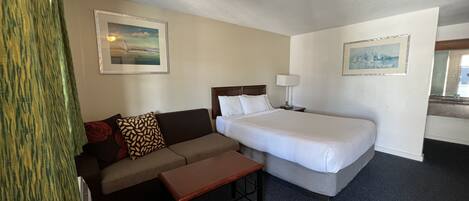A hotel room with a bed, a sofa, a small table, and two paintings on the walls.