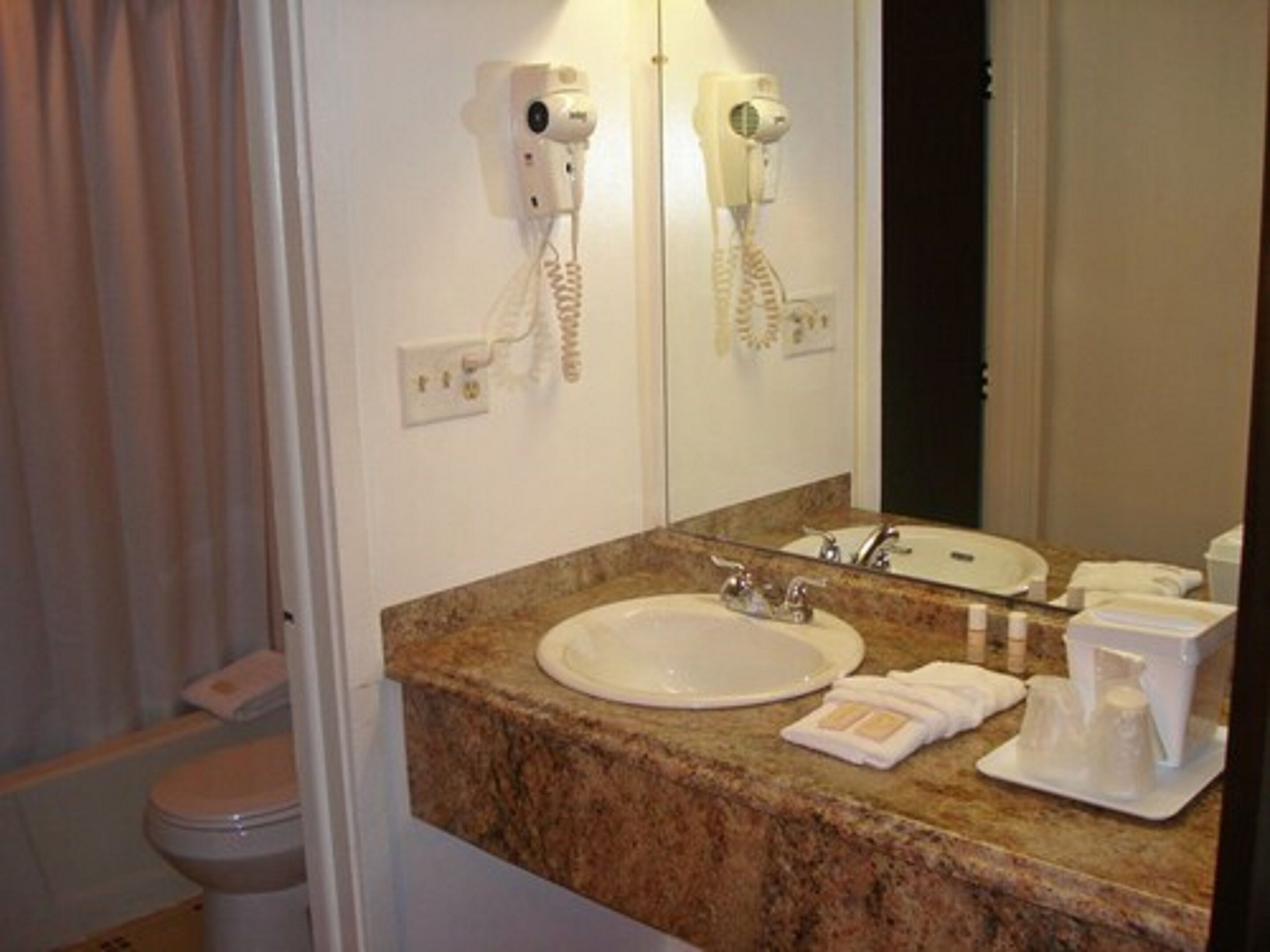 A bathroom with a marble sink, a mirror, a hairdryer, and a towel rack.