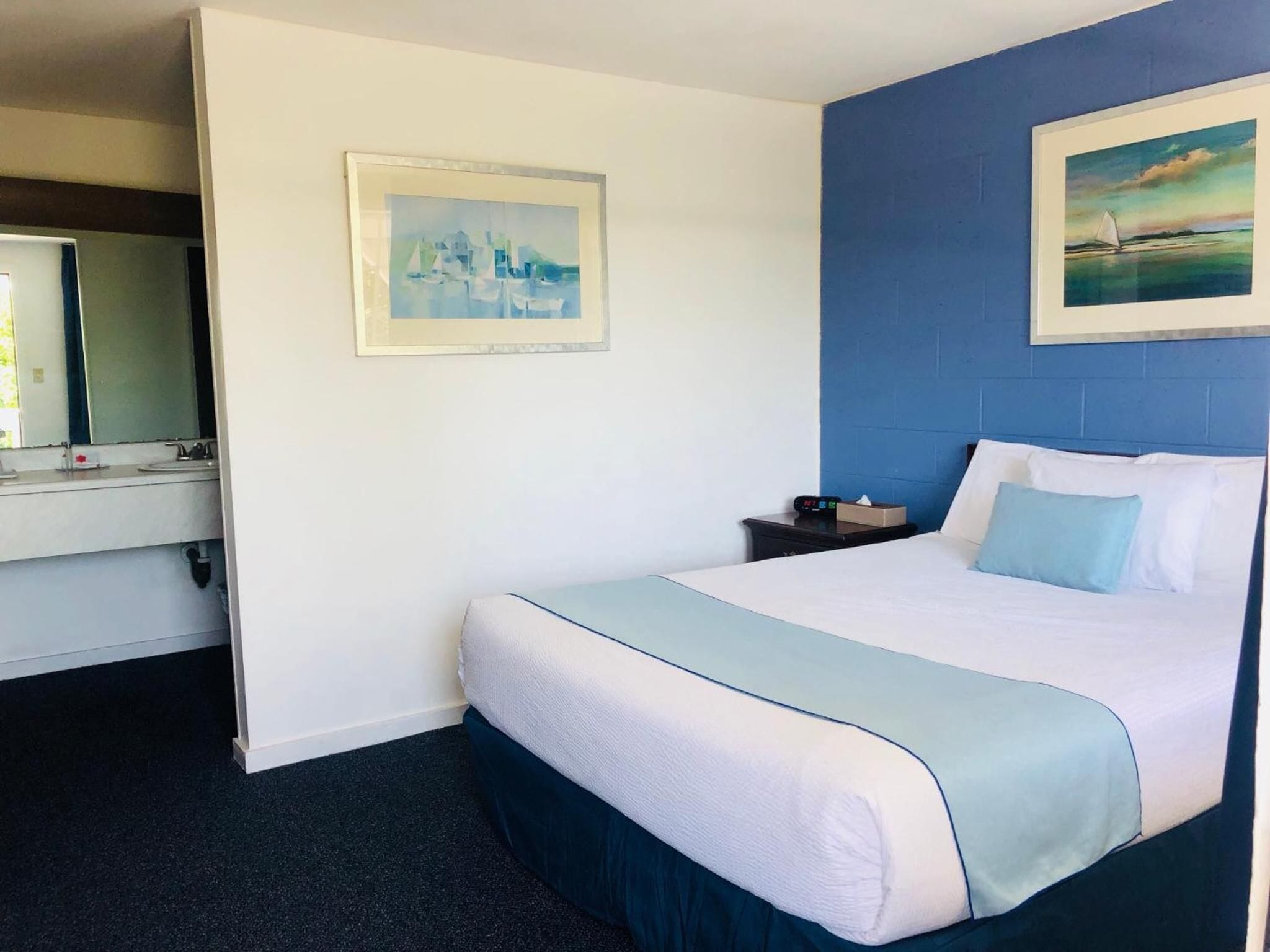 Une chambre d’hôtel avec un lit, une table de chevet, un miroir et deux tableaux accrochés aux murs.