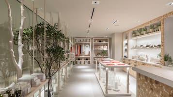 Una tienda minorista moderna con una mesa de exhibición central, estantes con productos y varios elementos decorativos como plantas y árboles.
