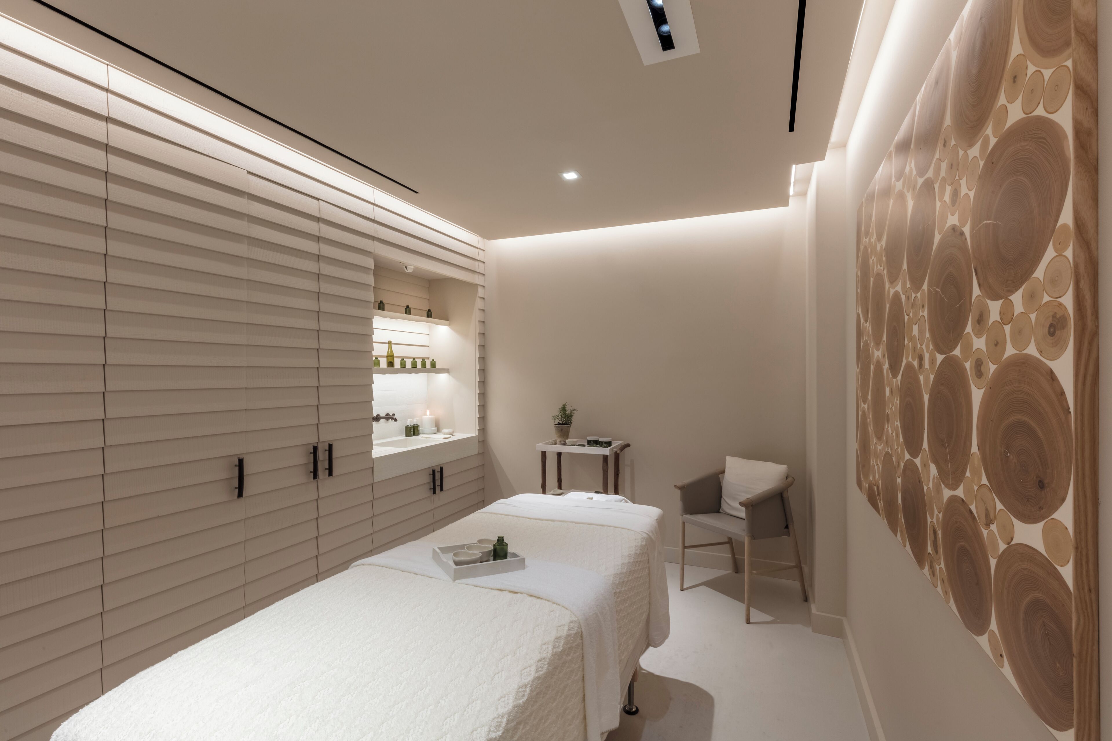 A modern spa room with a large bed, a small table with a plant, and a wall with a circular pattern.